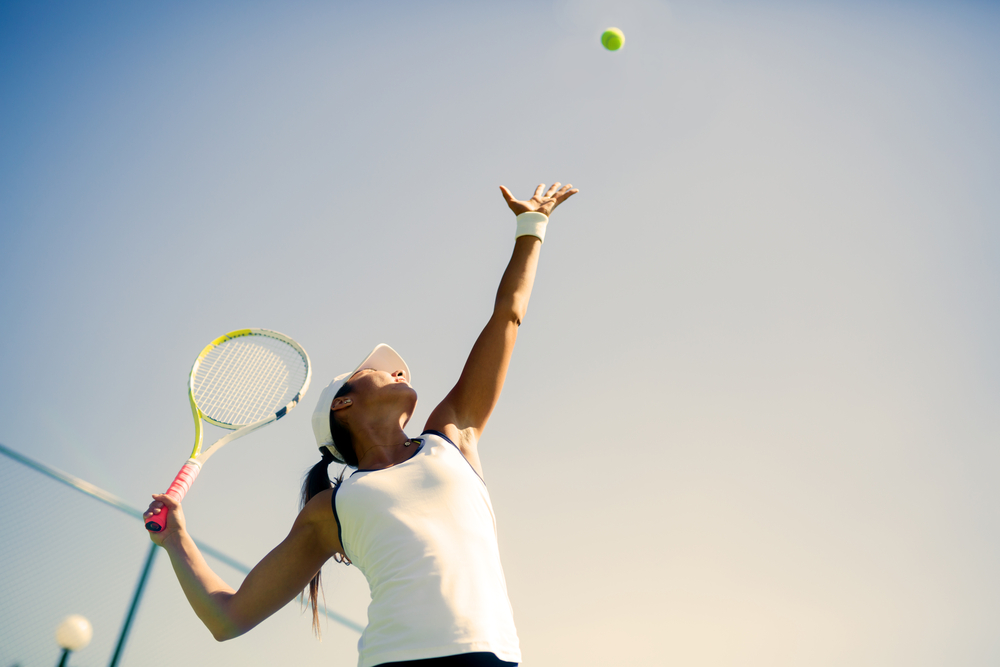 Mujer haciendo saque mientras juega al tenis